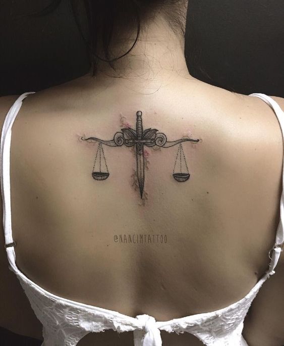 hình xăm một thanh kiếm ngắn và hai chiếc vảy trên lưng khách hàng hình xăm thanh kiếm ngắn và hai cán cân ở lưng chị khách